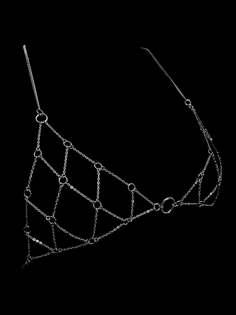 May include: A silver chain body jewelry piece with multiple interconnected rings. The chain is made of small, delicate links.