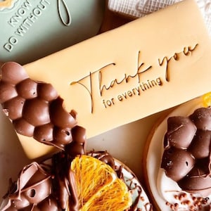 May include: A light brown rectangular biscuit with the text "Thank you for everything" in a handwritten font. The biscuit is decorated with chocolate and orange slices.
