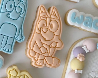 May include: A light pink cookie with a cartoon dog design. The dog is standing on all fours and has a light brown nose and black eyes.