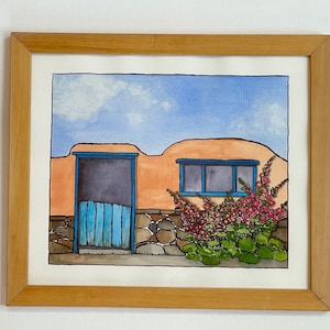May include: A watercolor painting of a small adobe house with a blue door and window. The house is surrounded by a stone wall and a bush of pink flowers.