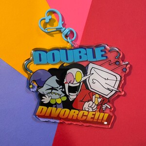 Puede incluir: Un llavero acrílico transparente con tres personajes de dibujos animados y las palabras "DOUBLE DIVORCE!!!" en azul y rojo. Tiene un cierre en forma de corazón azul claro. Fondo colorido.