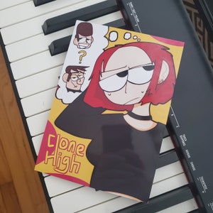 May include: A comic book cover with a yellow background and the title "Clone High" in red and white text. The cover features a cartoon character with red hair and a black shirt, looking thoughtful.
