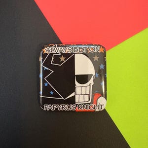 Peut inclure: Bouton carré avec un motif de crâne noir et blanc. Le bouton porte le texte "ALWAYS BET ON" en haut et "PAPYRUS KNIGHT" en bas. Le fond est un mélange de noir, de rouge et de vert.