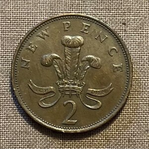 May include: A bronze-coloured two pence coin featuring the Welsh dragon with the inscription "NEW PENCE" around the edge.