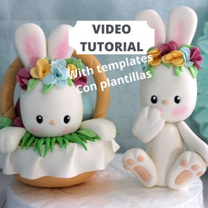 May include: Two white clay bunny figurines. One sits in a tan basket with green grass, colorful flowers, and eggs. The other sits beside it. Text reads: VIDEO TUTORIAL With templates Con plantillas. The bunnies have pink ears and cheeks.