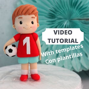 May include: A handcrafted figurine of a soccer player, wearing a red jersey with the number 1, blue shorts, and red shoes. The player is holding a black and white soccer ball. The image includes the text "VIDEO TUTORIAL" and "With templates Con plantillas".