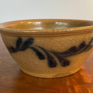 May include: A brown ceramic bowl with a blue and white floral design. The bowl is glazed and has a rustic look.