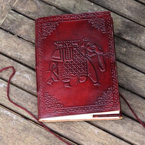 Peut inclure: Un carnet en cuir bordeaux avec un motif d'éléphant en relief. Le carnet a une bordure décorative et une fermeture en cuir.