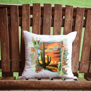 May include: White square pillow featuring a desert landscape design. The design includes a large green cactus, a sunset, and a turquoise outline of the state of Arizona. The pillow is decorated with cactus and floral accents.