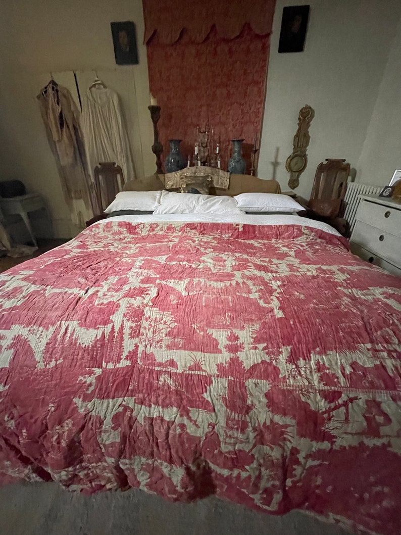 May include: A red and white patterned quilt with a floral design on a bed with white pillows.