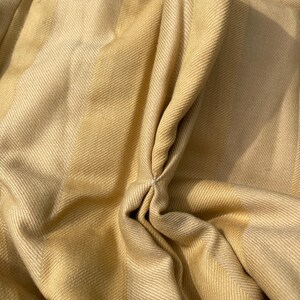 May include: Close-up of a beige and light brown striped fabric with a textured weave. The fabric is folded and gathered in the center, creating a soft, flowing look.