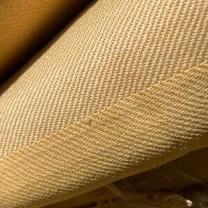 May include: Close-up of a yellow herringbone fabric. The fabric has a subtle texture and a soft, warm color.