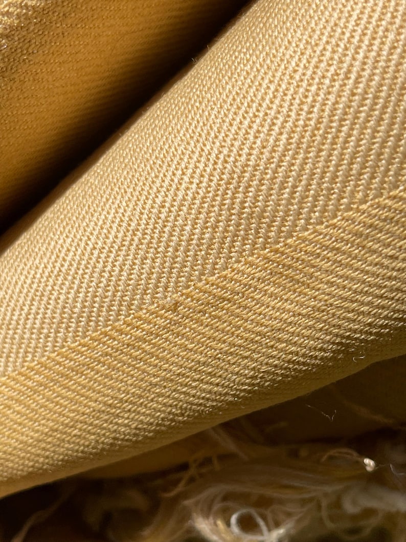 May include: Close-up of a yellow herringbone fabric. The fabric has a subtle texture and a soft, warm color.