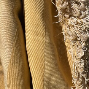 May include: A close-up of a mustard yellow woven throw blanket with a fringe border. The blanket has a herringbone pattern.