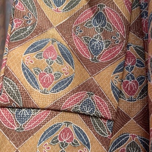 Puede incluir: Primer plano de una tela marr&oacute;n con un patr&oacute;n repetitivo de flores estilizadas en tonos rojos, azules y verdes. La tela tiene una textura sutil.