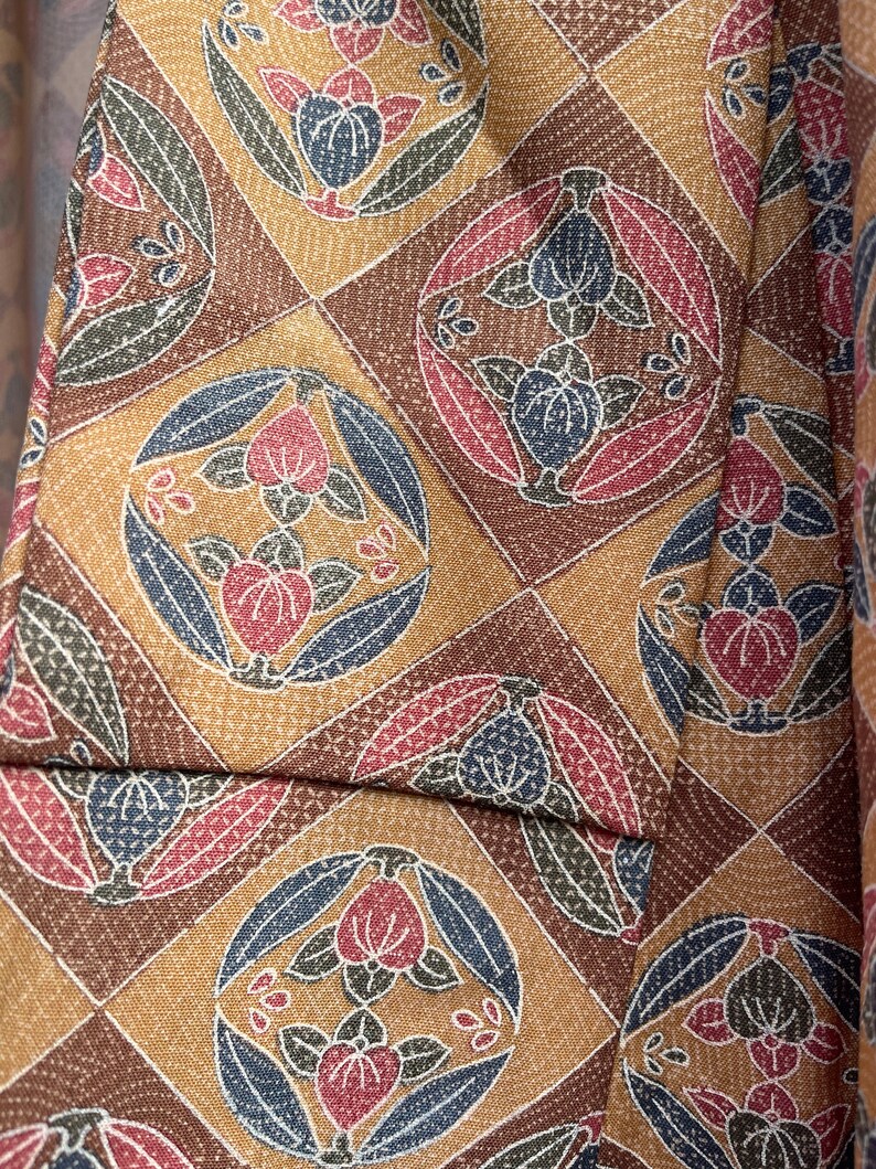 Puede incluir: Primer plano de una tela marr&oacute;n con un patr&oacute;n repetitivo de flores estilizadas en tonos rojos, azules y verdes. La tela tiene una textura sutil.