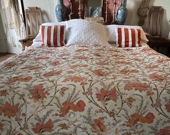 May include: A bed with a floral patterned quilt in shades of orange and cream. Two orange and white striped pillows and a white quilted pillow are on top of the bed. The headboard area features vases, a mirror, and candles.