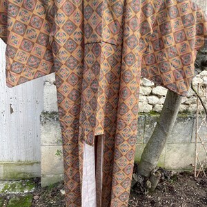 Puede incluir: Un kimono largo, marr&oacute;n y crema con un patr&oacute;n geom&eacute;trico. El kimono tiene cuello en V y mangas largas.