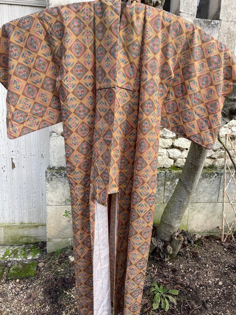 Puede incluir: Un kimono largo, marr&oacute;n y crema con un patr&oacute;n geom&eacute;trico. El kimono tiene cuello en V y mangas largas.