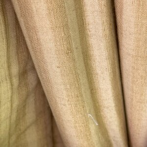 May include: Close-up of a beige fabric with vertical stripes. The fabric has a subtle texture and a slightly wrinkled appearance.
