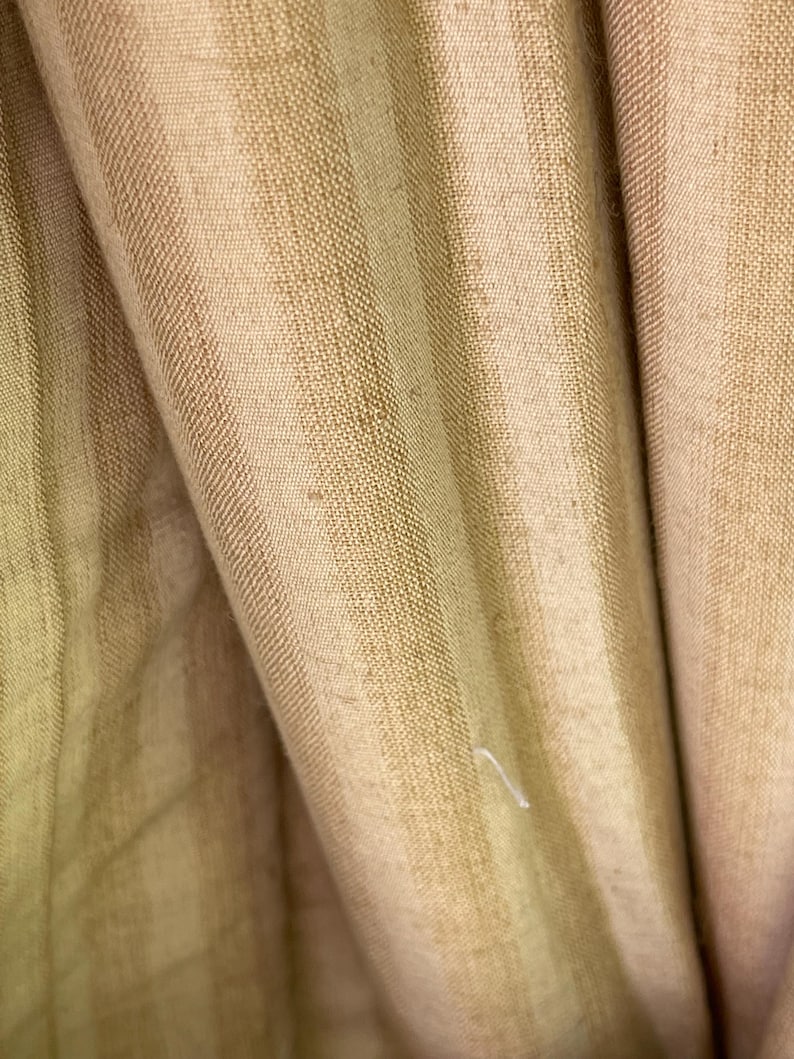 May include: Close-up of a beige fabric with vertical stripes. The fabric has a subtle texture and a slightly wrinkled appearance.