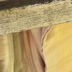 May include: A close-up of a wooden chair with a light brown and yellow fabric draped over it. The fabric has a striped pattern and a subtle sheen.