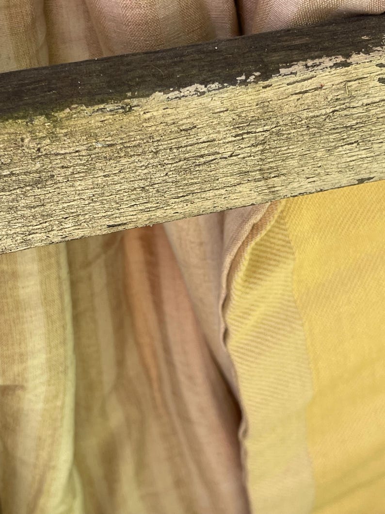 May include: A close-up of a wooden chair with a light brown and yellow fabric draped over it. The fabric has a striped pattern and a subtle sheen.