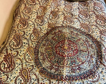 May include: A white bedspread with a paisley pattern in shades of red, blue, and yellow. The bedspread has a large circular design in the center.