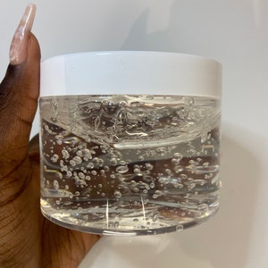 Peut inclure: Un pot en verre transparent avec un couvercle blanc rempli d'un gel transparent contenant de petites bulles d'air.