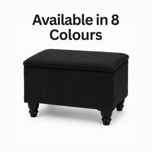 May include: A rectangular black storage ottoman with a flat top and four dark, rounded wooden feet. The text "Available in 8 Colours" is printed in black above the ottoman. The piece features a solid, uniform black fabric finish throughout.