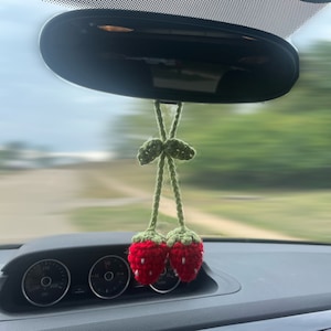 May include: Two red crocheted strawberries with green leaves hanging from the rearview mirror of a car.