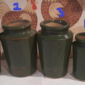 Może przedstawiać: Pięć zielonych ceramicznych słoików o różnych rozmiarach i wysokościach. Słoiki są wszystkie w głębokim zielonym kolorze i mają lekko fakturowaną powierzchnię.