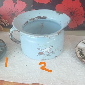 May include: A collection of three vintage items: a dark teal ceramic ashtray with embossed text, a light blue enamel chamber pot featuring a white goose illustration, and a round ceramic ashtray with the text Evening News Yorkshire.