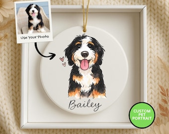 May include: A round, white ceramic ornament featuring a watercolor-style portrait of a Bernese Mountain Dog with the name "Bailey" below. The ornament has a gold string for hanging and is displayed in a white box. A small photo of the dog is also included.