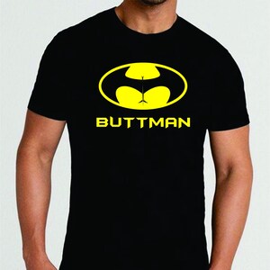 May include: Black t-shirt with a yellow logo that reads "BUTTMAN". The logo is a parody of the Batman logo, with a yellow oval and a stylized design. The shirt is short-sleeved and appears to be made of cotton.
