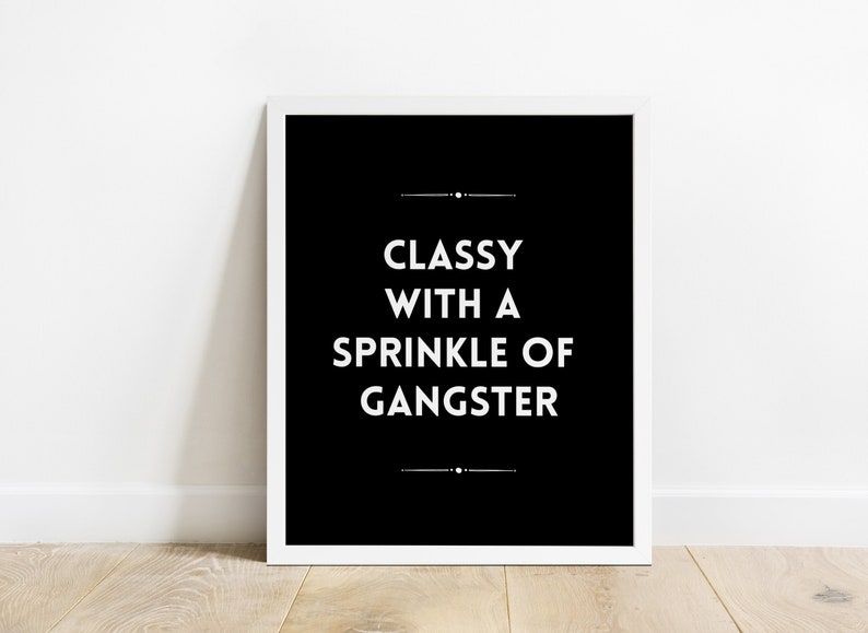 May include: A framed black and white print with the text "Classy with a Sprinkle of Gangster" in a bold, sans-serif font. The print is centered on a white background.