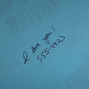 May include: A blue piece of paper with the handwritten message "I love you! 555-4823"