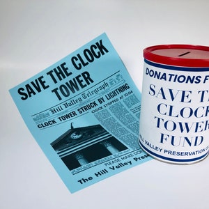 Può includere: Una scatola di donazioni bianca con un coperchio rosso e testo blu che recita "Donazioni per il Save the Clock Tower Fund". Un ritaglio di giornale blu con il titolo "Save the Clock Tower" e un'illustrazione in bianco e nero di una torre dell'orologio.