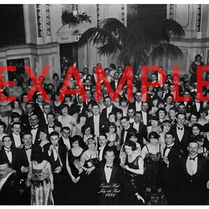 May include: A black and white photograph of a large group of people gathered in a ballroom. The people are dressed in formal attire and are smiling and laughing. The photo was taken at the Canadian Hotel on July 24th, 1921.