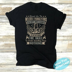 May include: Black t-shirt with a graphic design featuring a welder, wings, and text. The text reads "Blessed Are The Welder Fabricators The Dirty, Tired & Bloody For They Have Acquired The Skill To Create Something From Nothing."