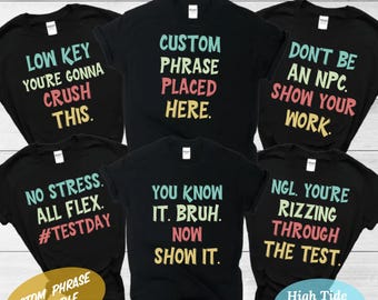 Könnte beinhalten: Sechs schwarze T-Shirts mit buntem Text. Die Shirts zeigen Sätze wie "Low Key You're Gonna Crush This", "Custom Phrase Placed Here", "Don't Be An NPC. Show Your Work", "No Stress. All Flex. #TestDay", "You Know It. Bruh. Now Show It", und "NGL. You're Rizzing Through The Test".