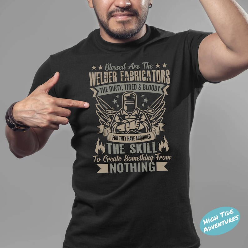 May include: Black t-shirt with a graphic featuring a welder and the text "Blessed Are The Welder Fabricators". The design includes wings, stars, and flames, with the phrase "The Skill To Create Something From Nothing".