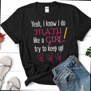 Può includere: Maglietta nera con il testo "Yeah, I know I do MATH like a GIRL... try to keep up!" in bianco con un cuore rosa e una grafica di lampadina.