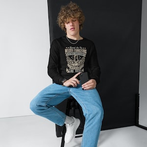May include: Black long-sleeve shirt with a graphic that reads "Blessed Are The Welder Fabricators The Dirty, Tired & Bloody For They Have Acquired The Skill." The shirt is worn with blue jeans and white sneakers.