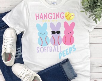 May include: White t-shirt with a graphic of three pastel-colored Easter Peeps holding baseballs. The text "Hanging with my Softball Peeps" is printed on the shirt.