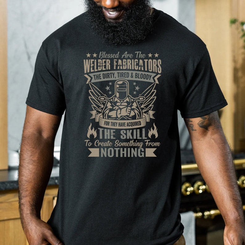 May include: Black t-shirt with a graphic design featuring a welder and the text "Blessed Are The Welder Fabricators." The design includes wings, stars, and the phrase "The Dirty, Tired & Bloody." The shirt also says "The Skill To Create Something From Nothing."