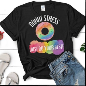 Può includere: Maglietta nera con un grafico di ciambella arcobaleno e il testo "Donut Stress Just Do Your Best!"