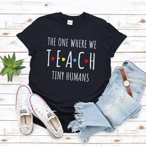 May include: Black t-shirt with white text that reads "The one where we teach tiny humans". The text "teach" has colourful dots around the letters.