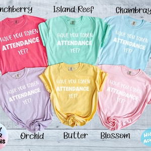 Può includere: Sei t-shirt a maniche corte in vari colori: Crunchberry, Island Reef, Chambray, Orchid, Butter e Blossom. Ogni maglietta ha il testo bianco "HAVE YOU TAKEN ATTENDANCE YET?". Le magliette sono su una superficie effetto legno chiaro.