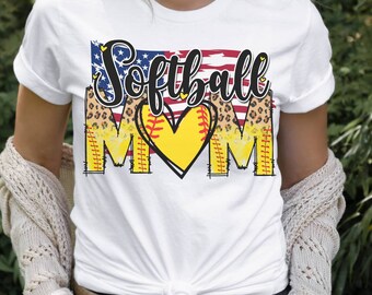 May include: White t-shirt with a graphic design featuring a softball, a heart, and the words "Softball Mom" with an American flag background.